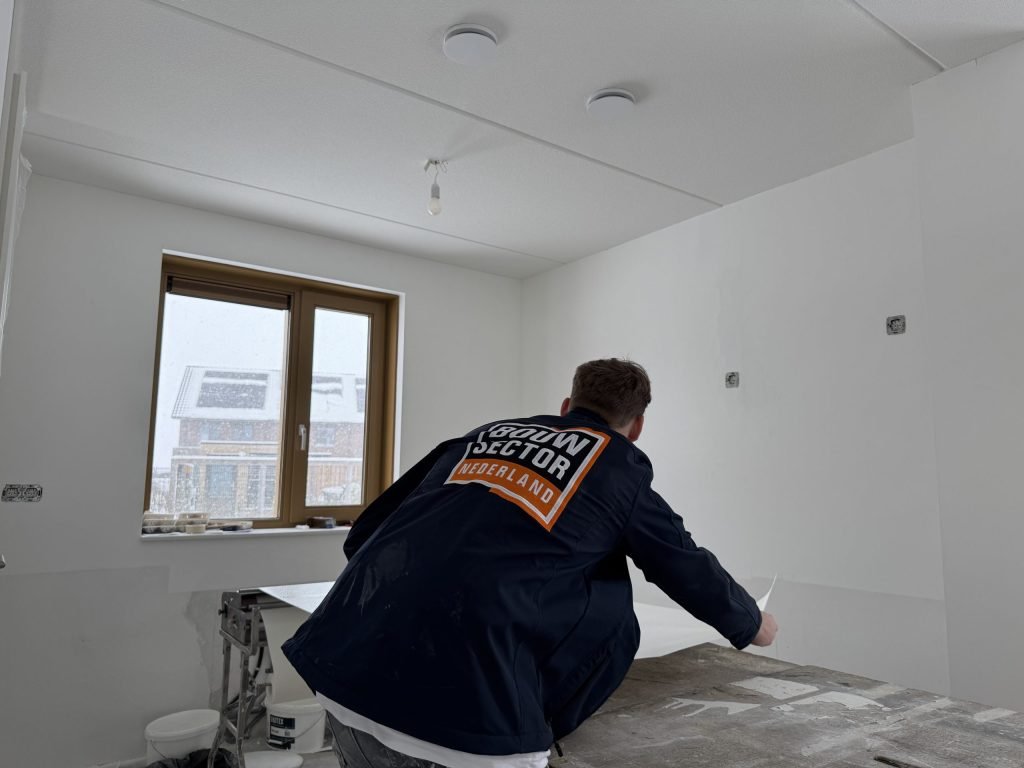 Vakman van Bouwsector Nederland legt een baan behang op de plaktafel in een kale kamer