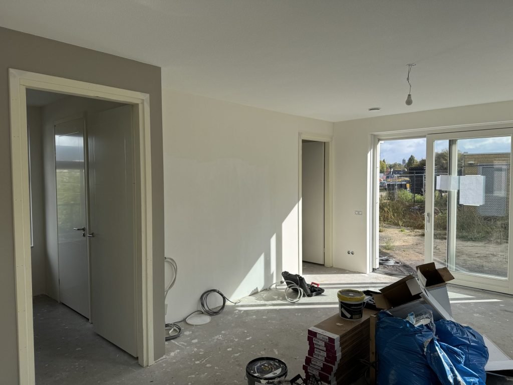 Nieuwbouwwoonkamer tijdens de afwerking, met verfemmers en materiaal op de vloer