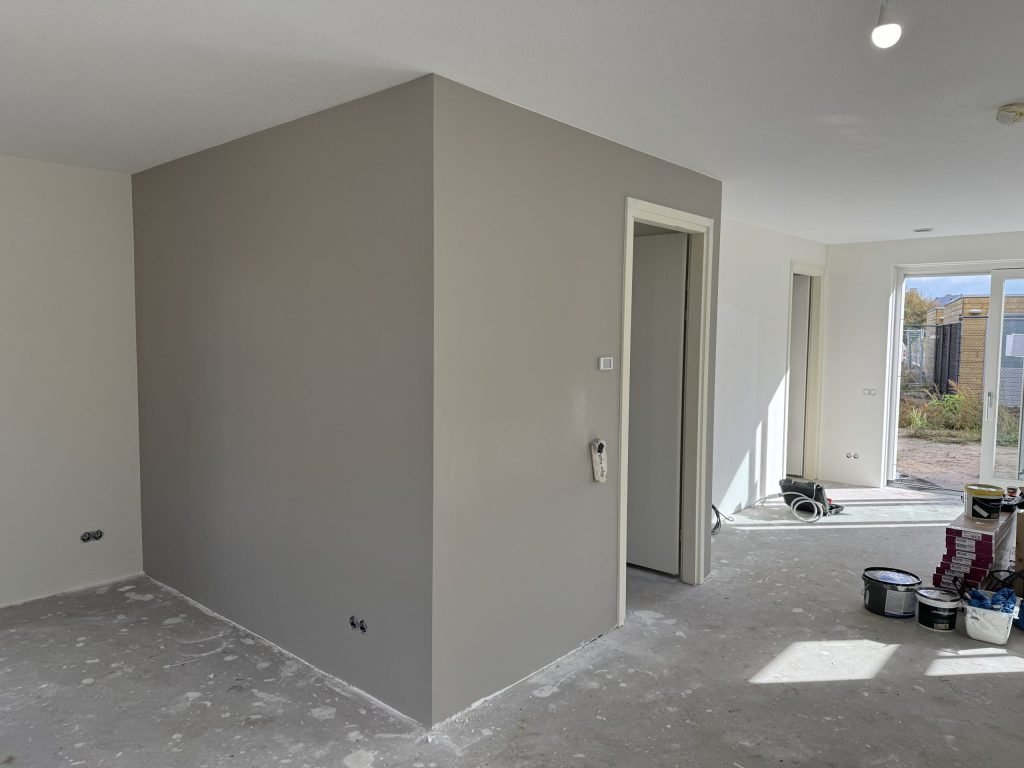 Nieuwbouwwoning met een pas afgewerkte grijze wand en verfemmers op de vloer