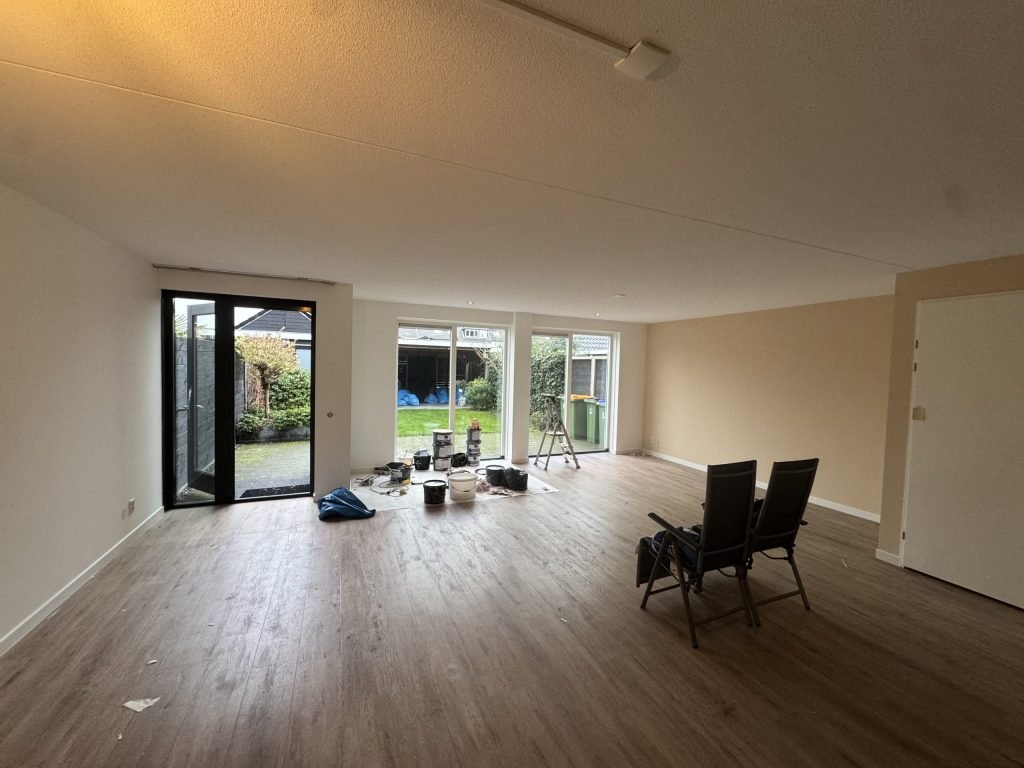 Ruime woonkamer met lichte, gesausde wanden, een houten vloer en tuindeuren